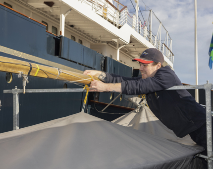 A Maintenance team member is putting a cover over a small yacht on Britannia's Quayside. 
