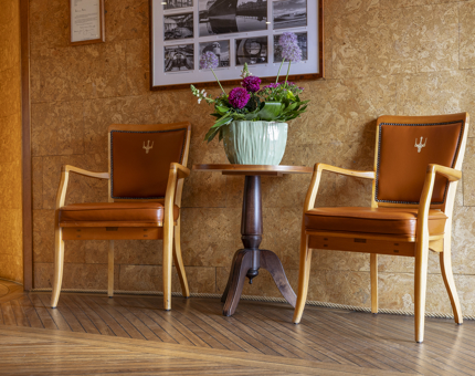 In the entrance to Fingal Hotel, two brown chairs, with a small table between them is situated against a wall, it has a green pot with pink flowers in it. 