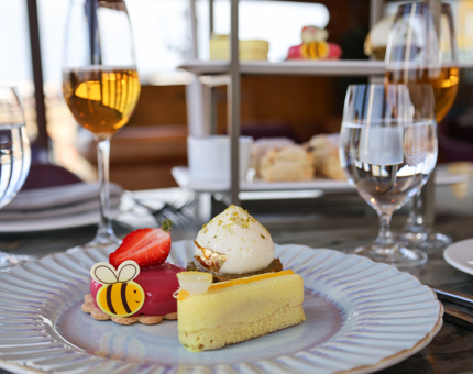 A plate with Easter themed sweet treats from the afternoon tea in The Lighthouse Restaurant. There are glasses with sparkling tea in them. 