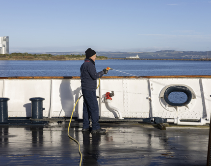 A man hosing down the decks of Britannia, Port of Leith in the background. 
