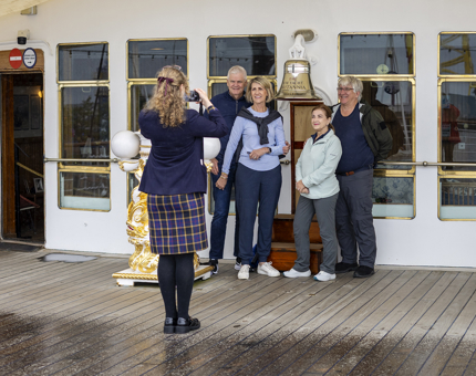 A Visitor Assistant is taking a photo of four visitors at Britannia's Bell on the Verandah Deck. 
