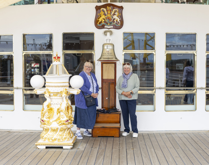  Two Visitors pose for a photo at Britannia's Bell and binnacle on the Verandah Deck. 