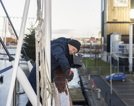 A Maintenance team member leaning over a railing to apply a coat of paint. 