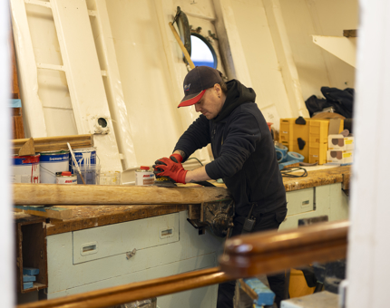 A maintenance team member is sanding a wooden handrail. 
