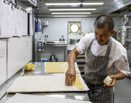 A chef is in Britannia's Galley cutting out pastry on trays. 