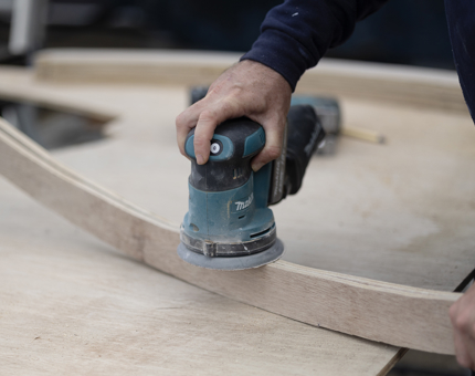 A closer look at a hand holding an electric sander, sanding wood. 