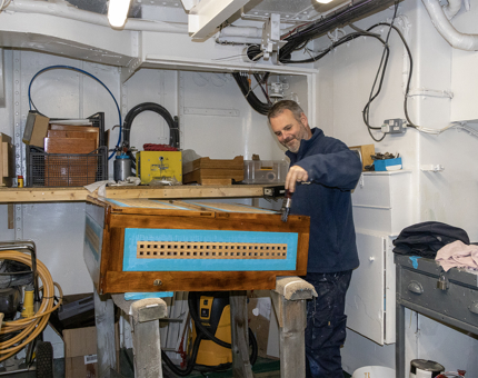 A man from the Maintenance Team painting varnish onto a wooden rope box. 