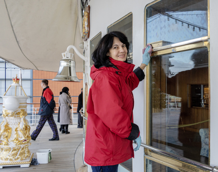 A woman from the Housekeeping team polishing the brass outside the Sun Lounge on the Verandah Deck. 