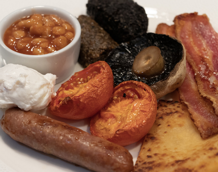 A full Scottish breakfast of eggs, tomatoes, baked beans, bacon, sausage and hash brown. 