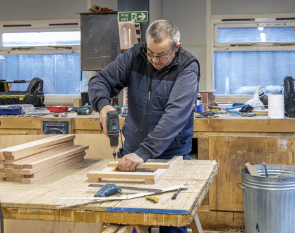 A man drills wood to screen a sign together. 