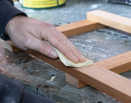 A member of the Maintenance Team sanding a wooden frame for a sign. 
