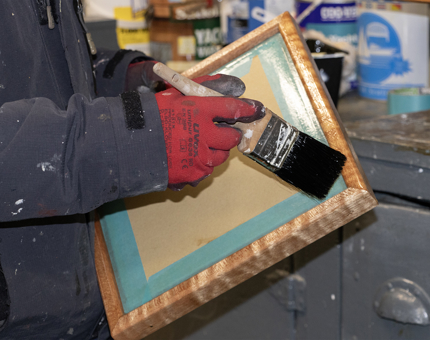 Hand with paint brush varnishing wood 