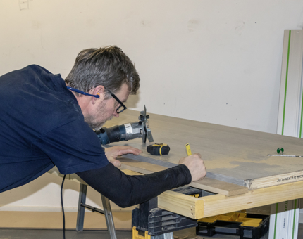 A man marking out panels to cut on a wooden workbench. 