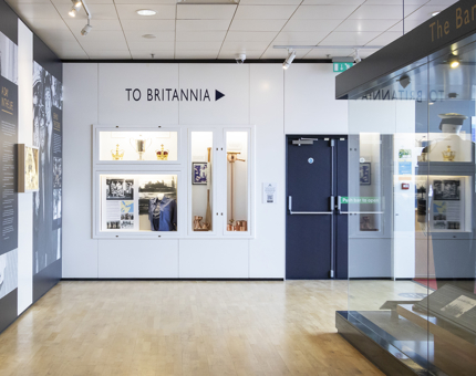 Inside Britannia's Visitor Centre with display cabinets on the wall containing uniform and objects of interest. 