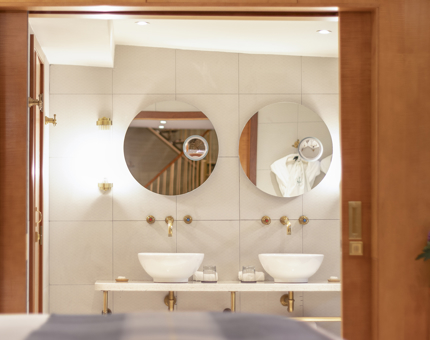 The bathroom in a luxury duplex cabin at Fingal. There are twin wash basins and circular mirrors. Wooden sliding doors separate the bathroom from the sleeping area. 