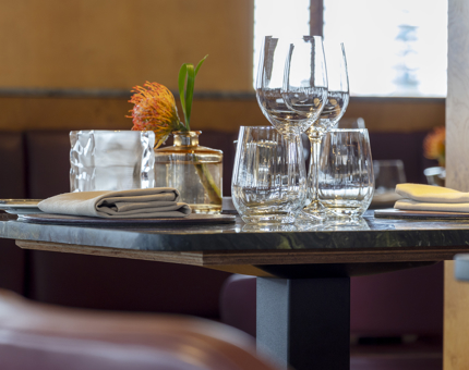A table in Fingal's Lighthouse Restaurant & Bar is set for dining. There are glasses, a linen napkin and a vase with an orange flower on the table. 