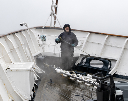 A member of Maintenance standing smiling stops mid-washing of the Fo'c'sle. 