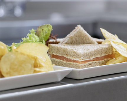 A plate containing a smoked salmon sandwich, crisps and salad. 