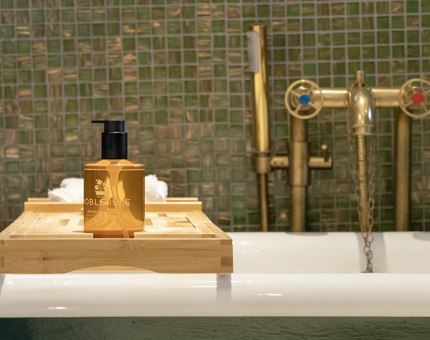A bathtub in a cabin at Fingal. There is a wooden bath tray containing a bottle of body wash. 