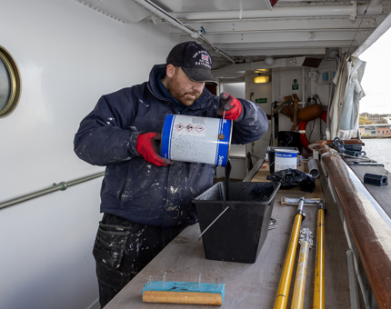 A man pouring blue paint into a bucket to prepare for painting. 