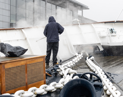 A man washing down the Fo'c'sle Deck. There are large anchor chains on the deck. 