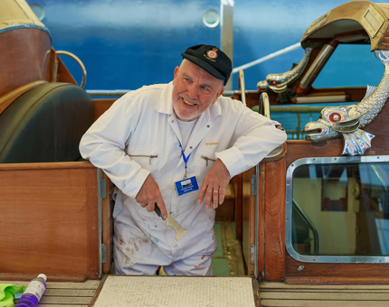 A Yottie standing smiling on the Royal Barge holding a paint scraper. 