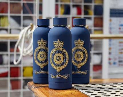Three navy water bottles with gold crest detail are pictured in front of the flag locker.