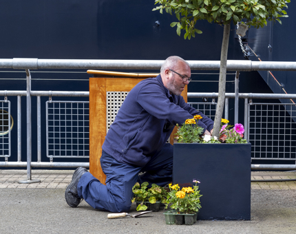 A man from the Facilities team planting flowers in a large planter on the quayside. 