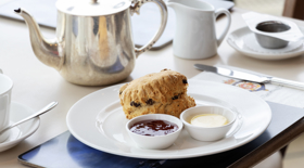 A table in the Royal Deck Tearoom containing a scone, jam, cream and a silver pot of tea. 