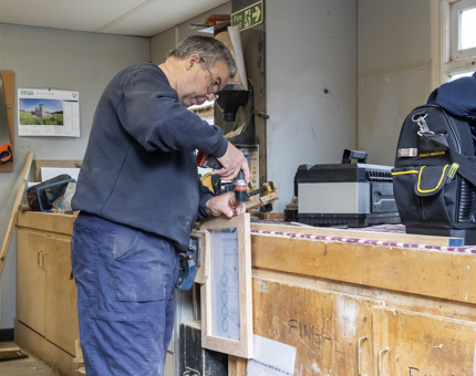 A man in the Maintenance team workshop is assembling wooden cabinet doors. 