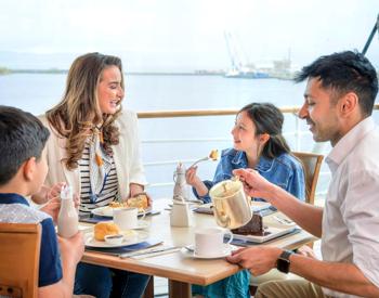 Family enjoying cream tea together on Royal Britannia ship family-friendly attraction in Edinburgh in The Royal Deck Tearoom, a fun thing to do in Edinburgh with kids