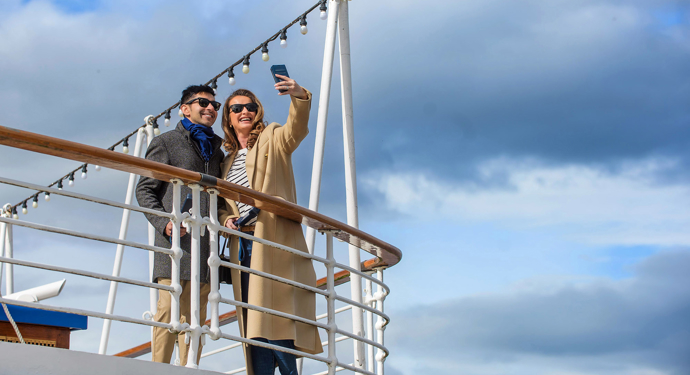 A man and a woman pose for a selfie outside on deck. 