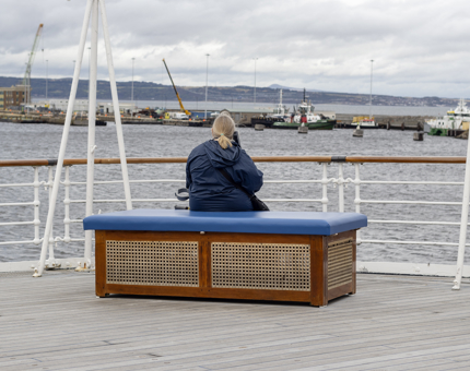 A woman visitor is sitting on the Verandah Deck listening to an audio guide looking out at the view.
