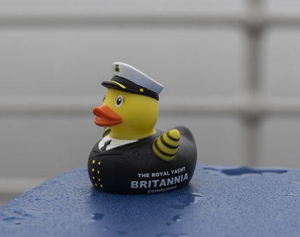 A rubber duck in a captains uniform sitting in the rain. 