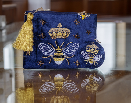 A blue velvet pouch with an image of a bee on it and a gold tassel. 