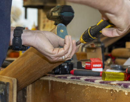 A close up of hands holding a screw driver fixing a brass end onto a handrail. 