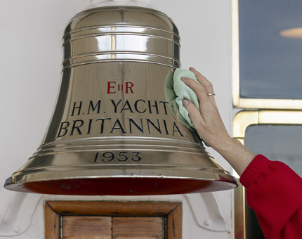 A close-up of a hand cleaning a large silver bell. 