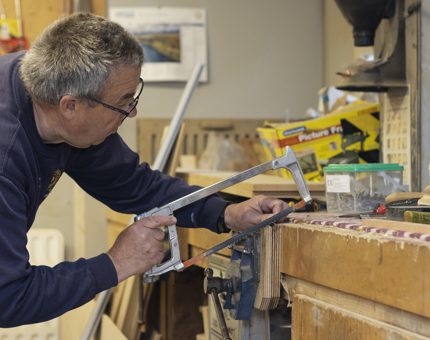 A man holding a handsaw cutting a hinge to size. 