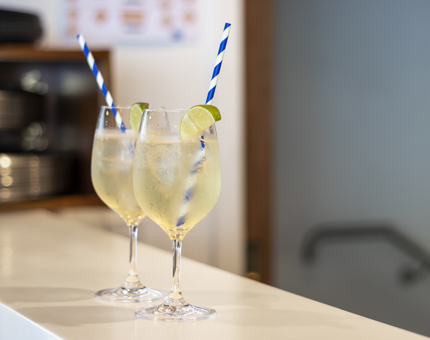 two glasses of spritz with blue and white straws on the bar counter waiting to be served. 