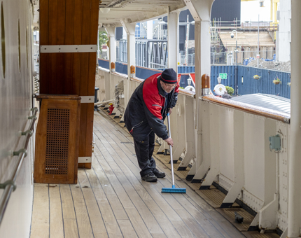 A man holding a broom sweeping the deck. 