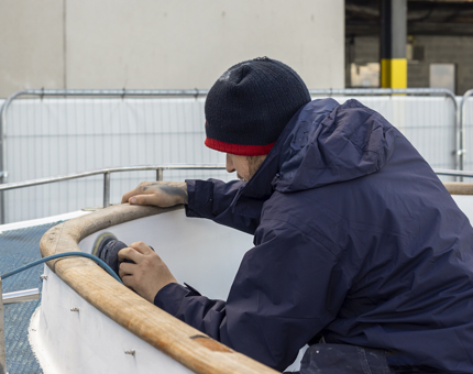 A man wearing a blue jumper sanding the Activity boat. 