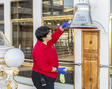 A woman in a red top polishing a silver bell. 