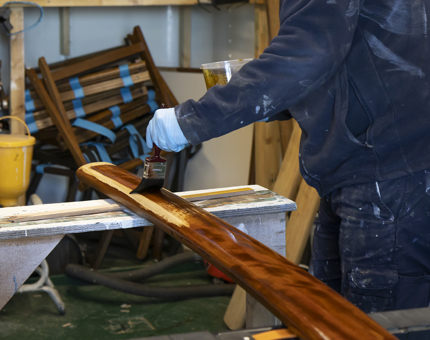 A hand holding a paint brush varnishing a handrail.