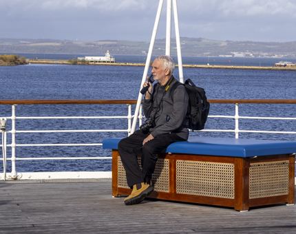 A man sitting on the Verandah Deck listening to the audio guide handset. 