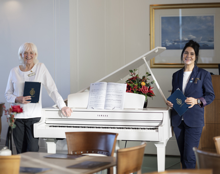 Two Tearoom team members pose by a white grand piano. 