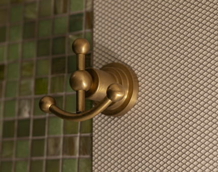 A hook on a green tiled bathroom wall shaped like an anchor. 