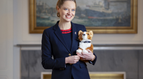 A woman standing in the Drawing Room holding a corgi plush toy. A woman standing in the Drawing Room holding a corgi plush toy.