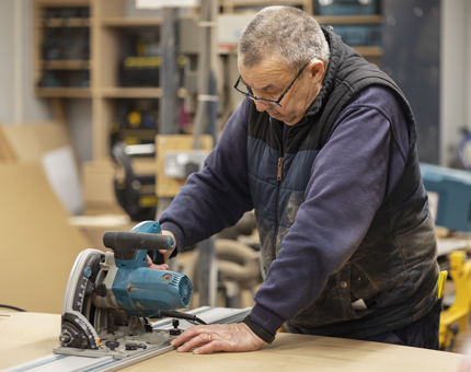 A Maintenance team member cutting wood in the Joiner's Workshop. 