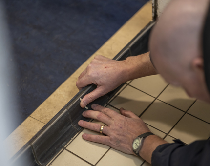 A member of the Maintenance team laying tiles on the Galley floor. 