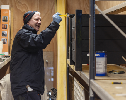 A Facilities Officer paints a wooden planter dark blue. 
